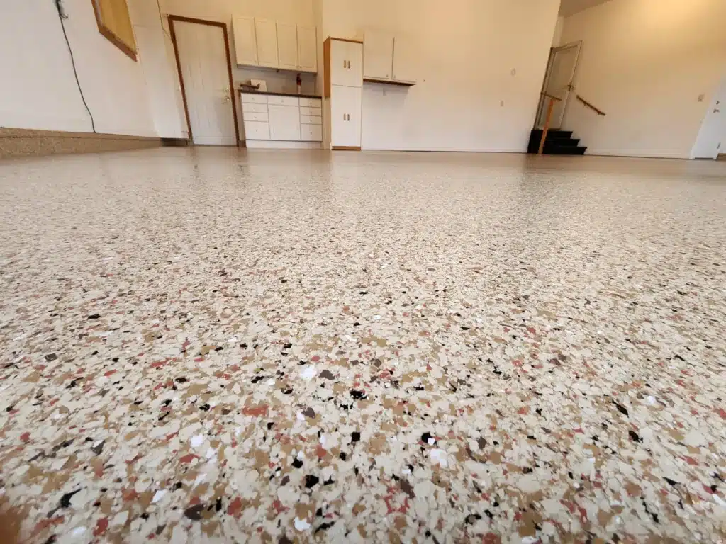 An empty room with speckled terrazzo flooring, white cabinetry, and a staircase at the back. The space appears clean and unoccupied.