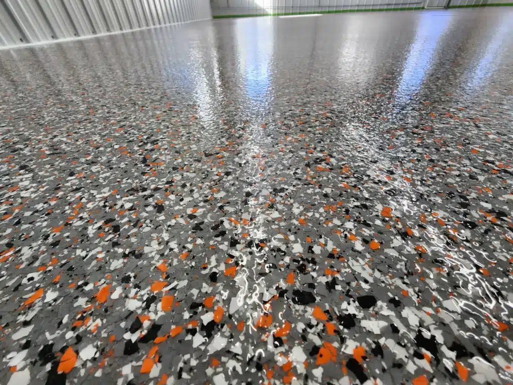 This image features a glossy, speckled floor with a high shine, reflecting industrial-style metal walls in a spacious, empty interior space.